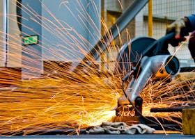 A worker operates a grinder cutting metal, creating a vibrant display of sparks in an industrial setting.
